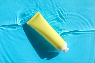 Tube with moisturizing cream in water on light blue background, top view