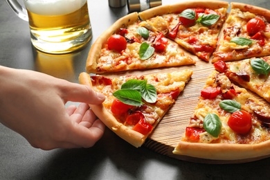 Man taking slice of delicious pizza with tomatoes and sausages at table