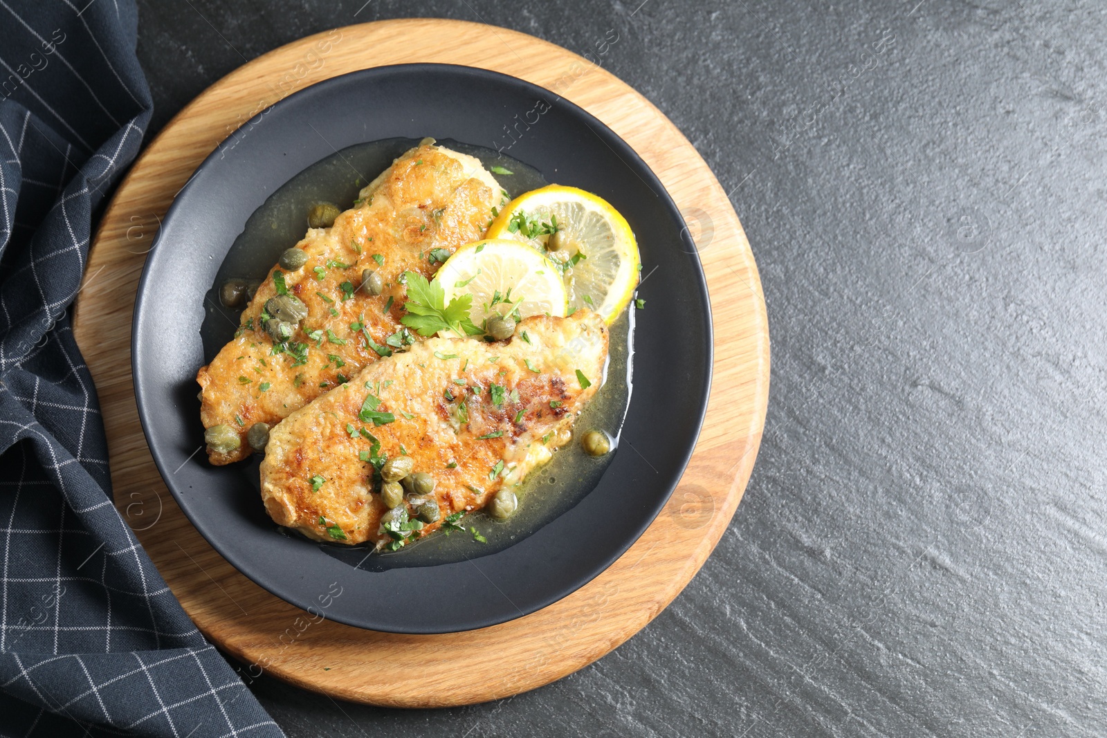 Photo of Delicious chicken piccata on black table, top view