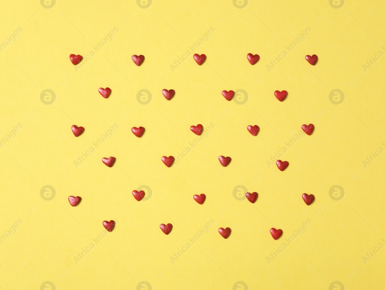 Photo of Bright heart shaped sprinkles on yellow background, flat lay