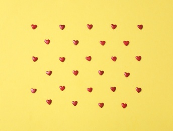 Photo of Bright heart shaped sprinkles on yellow background, flat lay