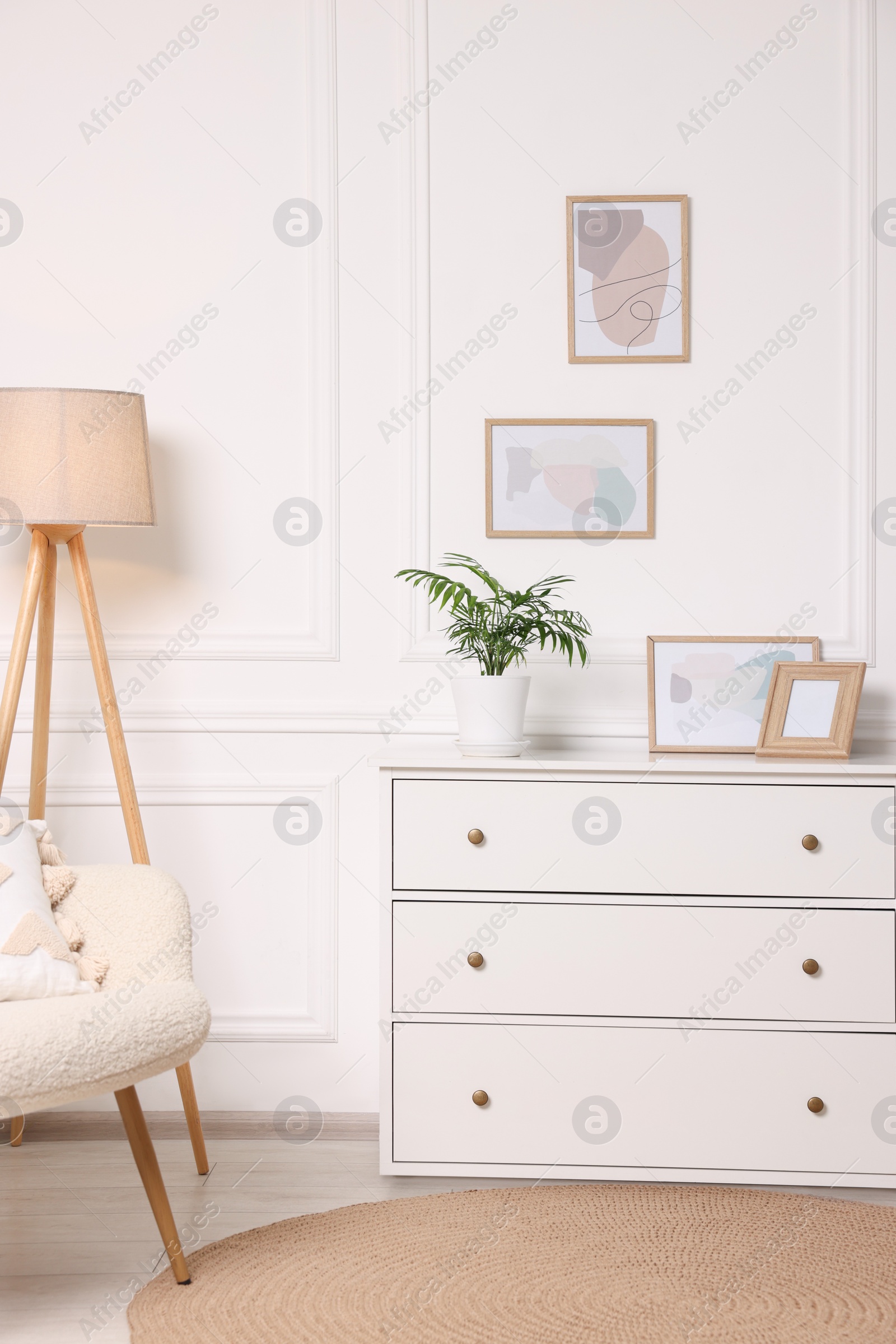 Photo of Picture frames hanging on white wall and chest of drawers at home