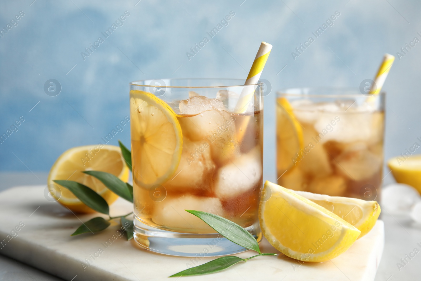 Photo of Glasses of lemonade with ice cubes and fruit on table against color background