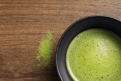 Photo of Cup of fresh matcha tea and green powder on wooden table, top view. Space for text