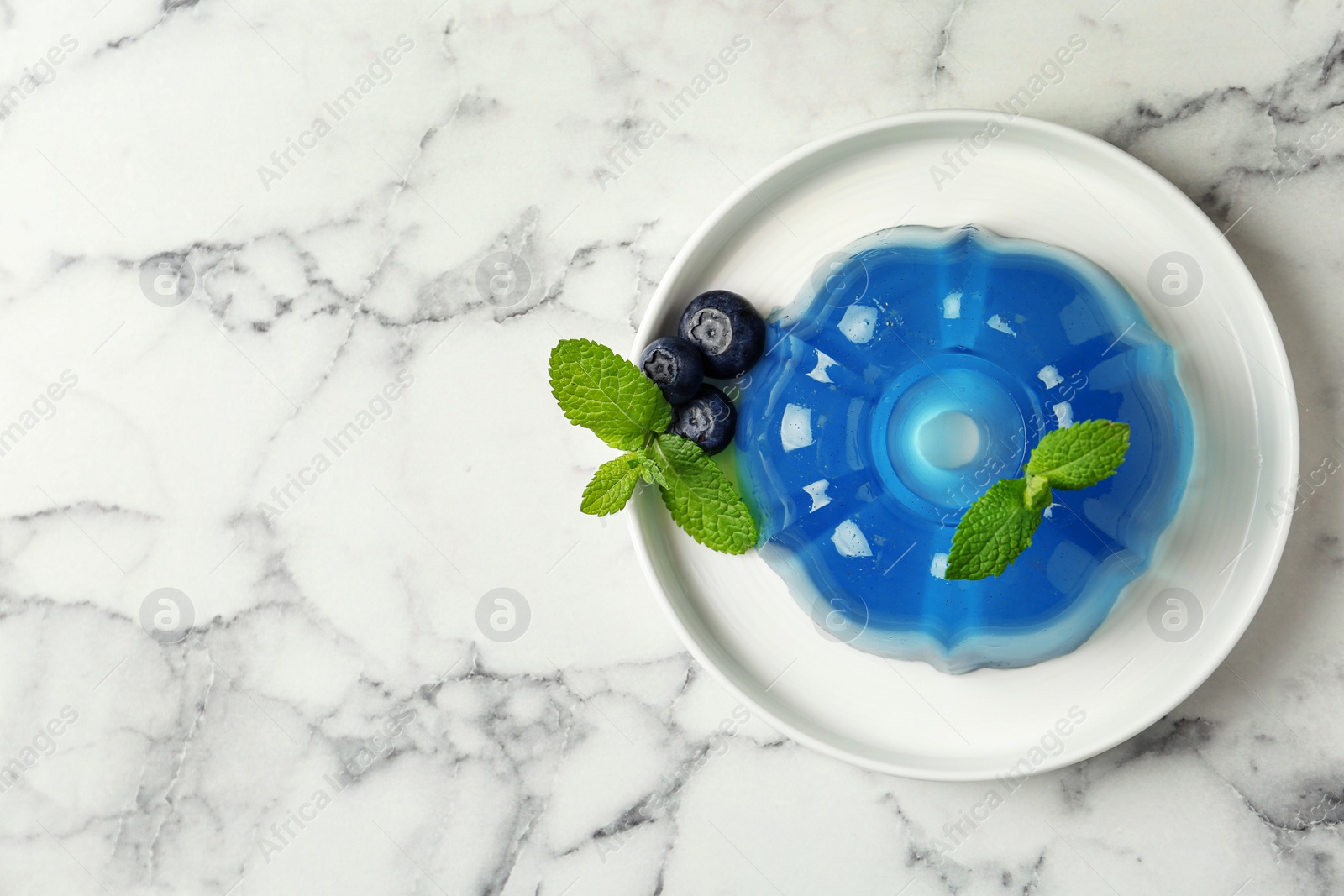 Photo of Plate of delicious blue jelly with berries on marble background, top view. Space for text