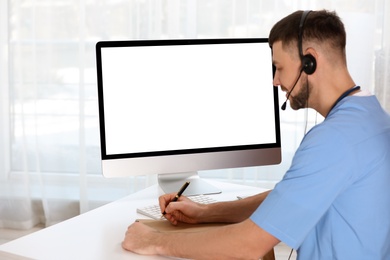 Doctor with headset consulting patient online at desk in clinic, space for text. Health service hotline