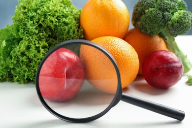 Photo of Fresh fruits, vegetables and magnifying glass on white table, closeup. Poison detection
