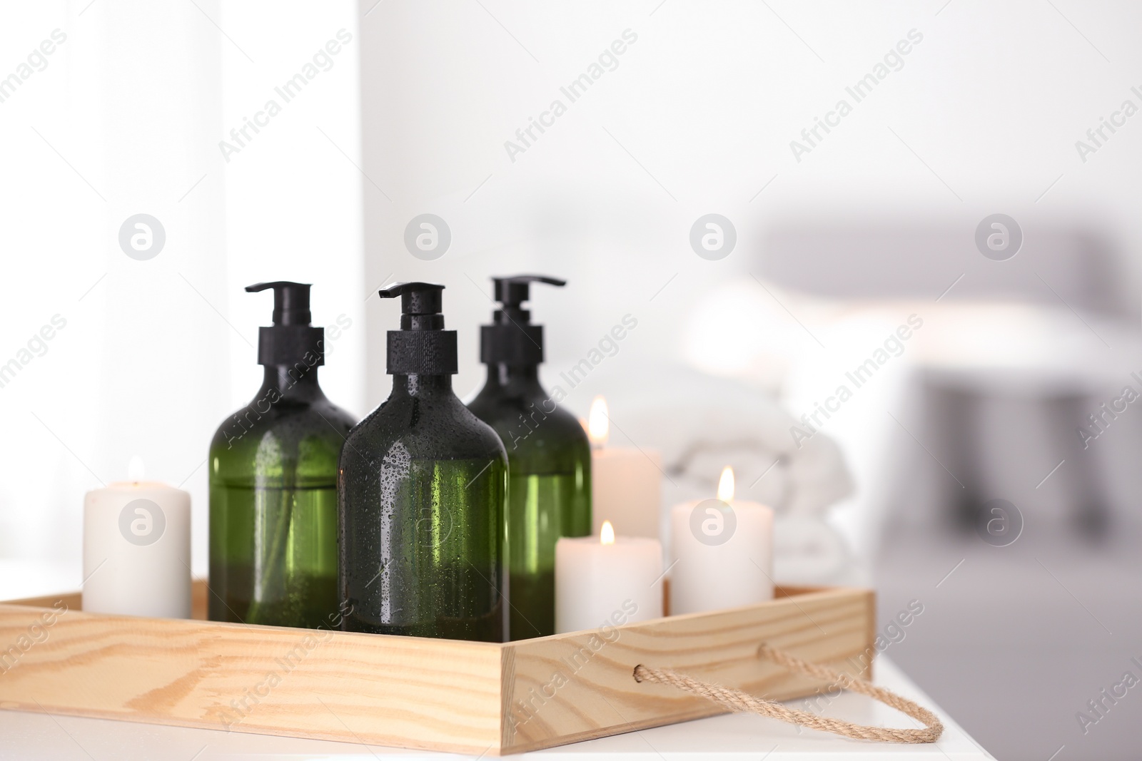 Photo of Wooden tray with soap dispensers and burning candles on white table. Space for text