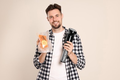 Smiling man holding sous vide cooker and salmon in vacuum pack on beige background