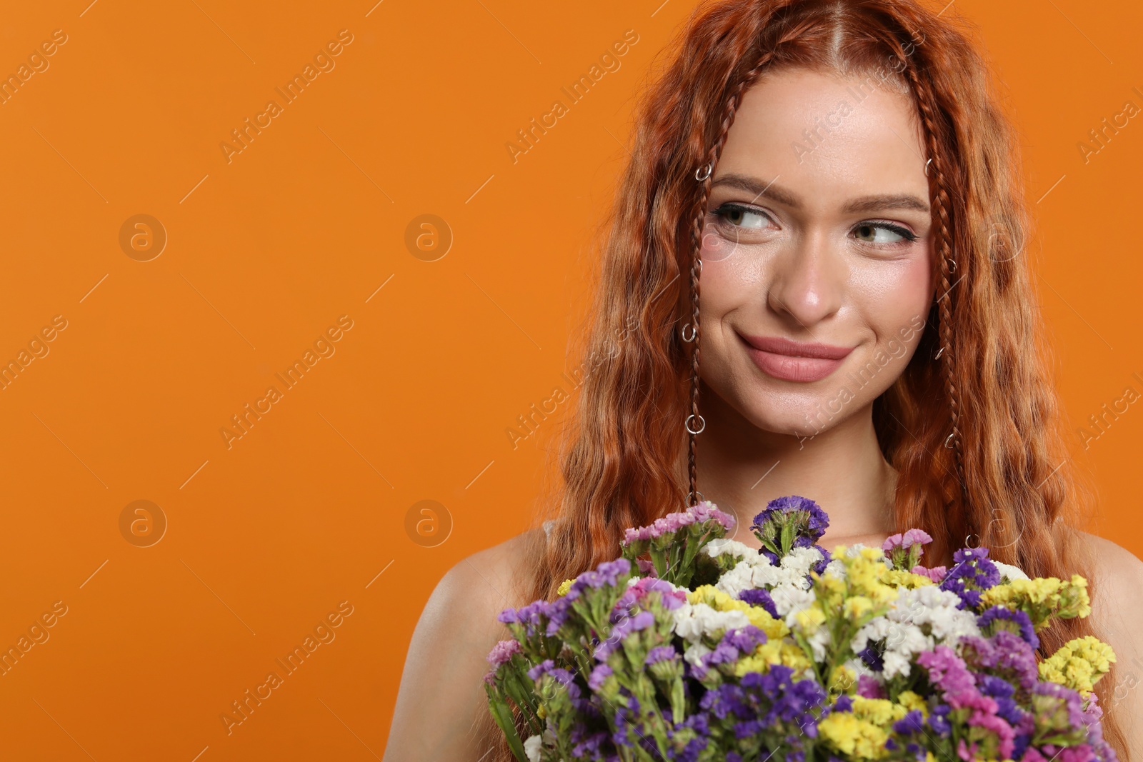 Photo of Beautiful young hippie woman with bouquet of colorful flowers on orange background, space for text