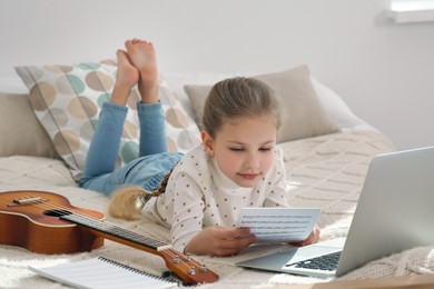 Photo of Little girl learning to play ukulele with online music course at home. Time for hobby