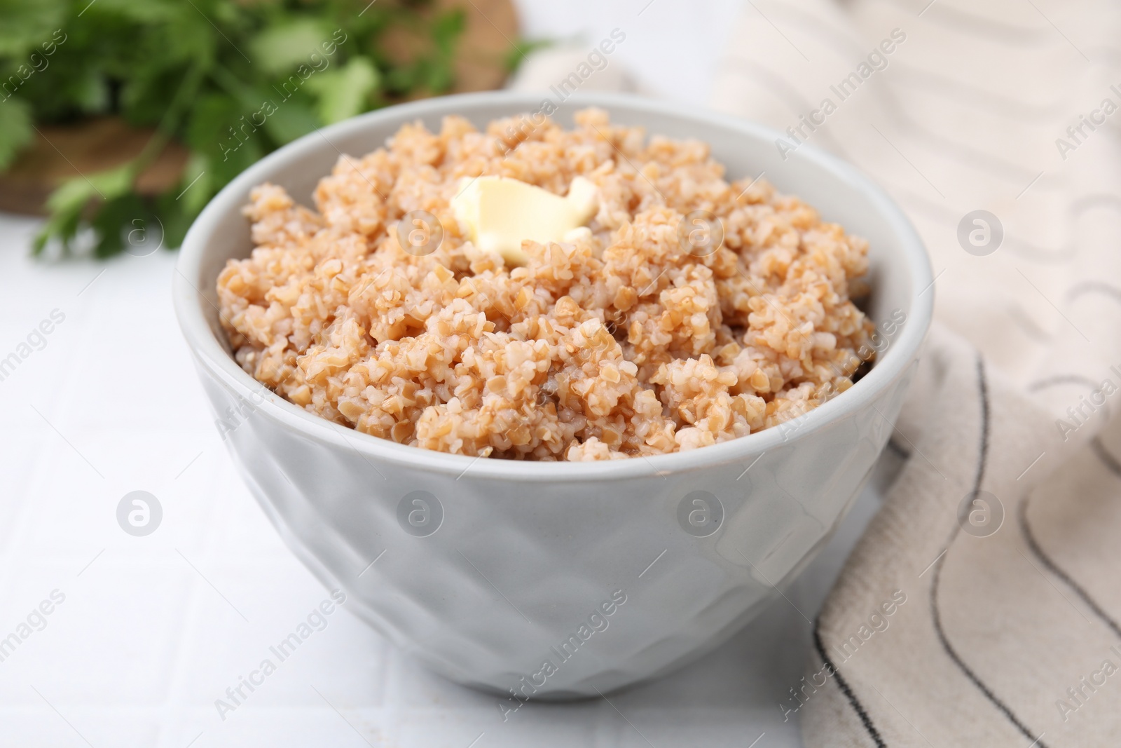 Photo of Tasty wheat porridge with butter in bowl on white tiled table, closeup