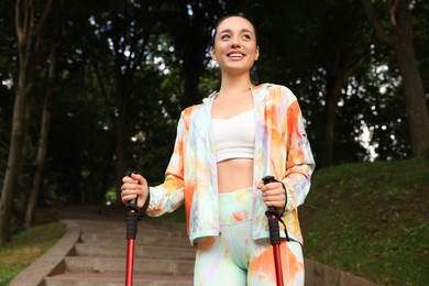 Young woman practicing Nordic walking with poles on steps outdoors, low angle view