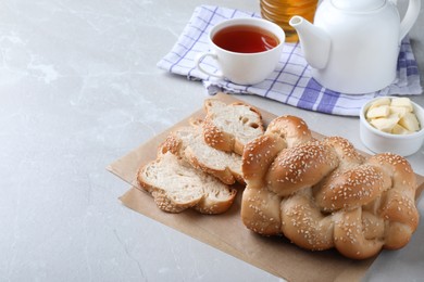 Photo of Cut homemade braided bread and freshly brewed tea on light grey table, space for text. Traditional Shabbat challah