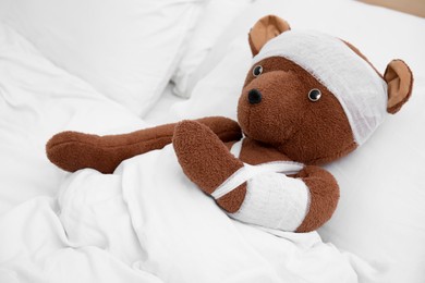 Photo of Toy bear with bandages lying in bed