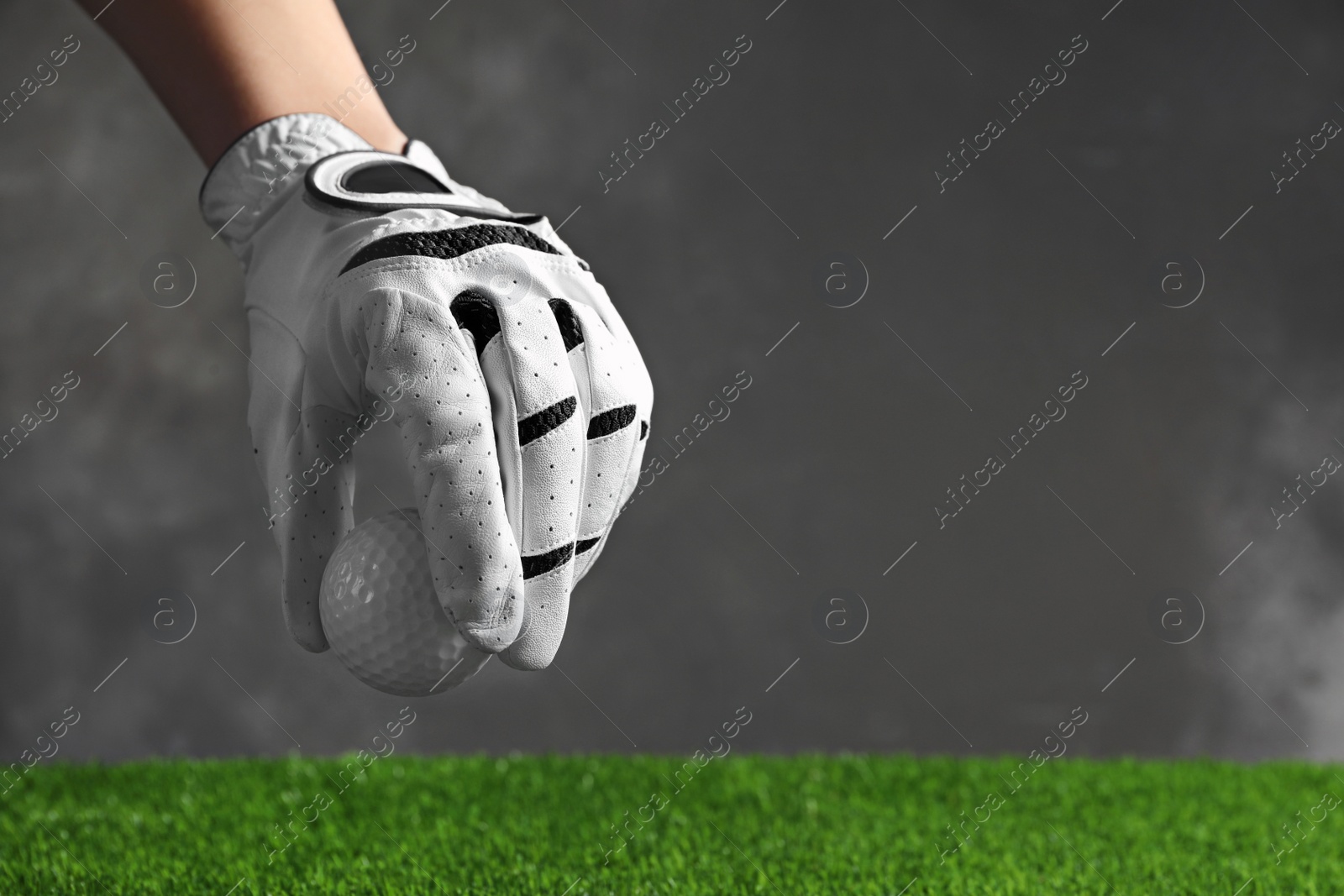 Photo of Person putting golf ball on green grass against grey background, closeup with space for text