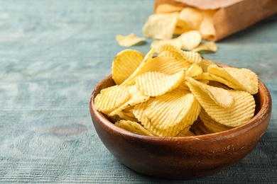 Delicious crispy potato chips in bowl on table, space for text