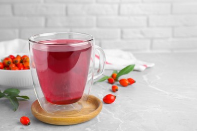 Aromatic rose hip tea and fresh berries on light grey marble table, space for text