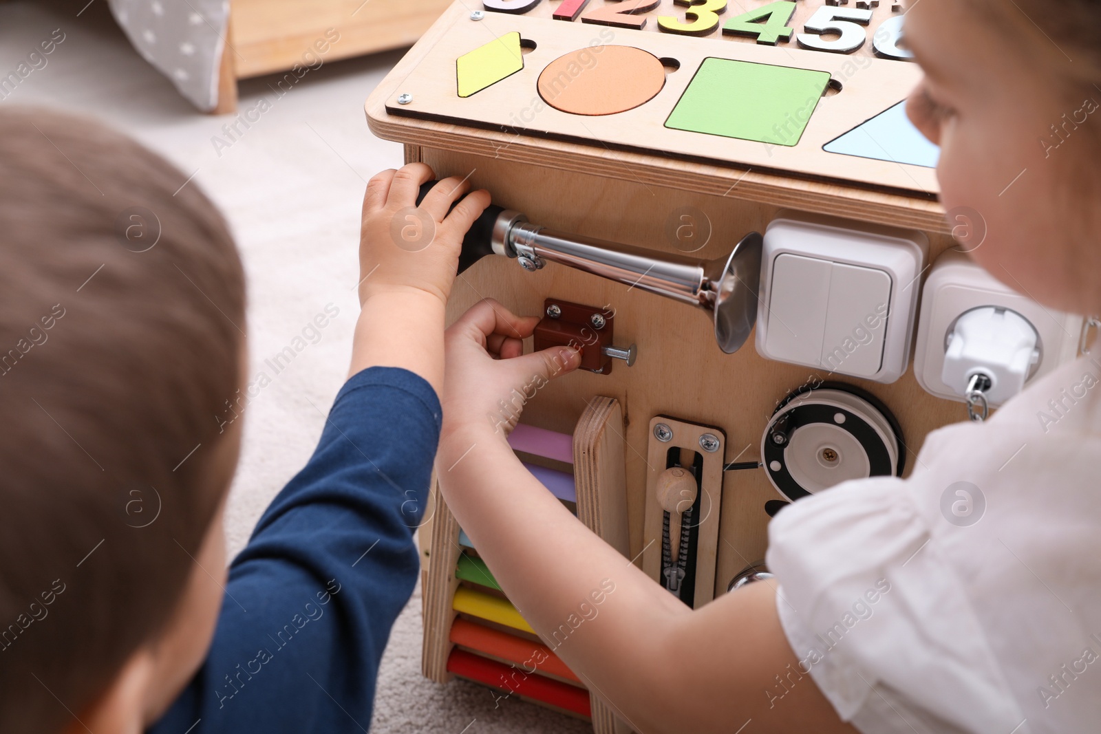 Photo of Little boy and girl playing with busy board house on floor in room