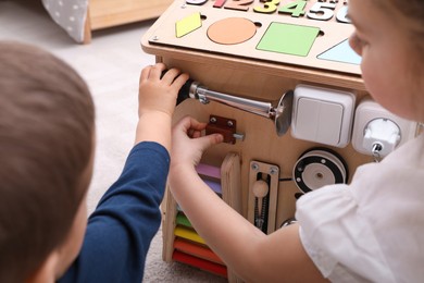 Photo of Little boy and girl playing with busy board house on floor in room