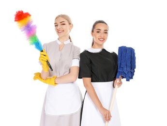 Young chambermaids with dusting brush and mop on white background