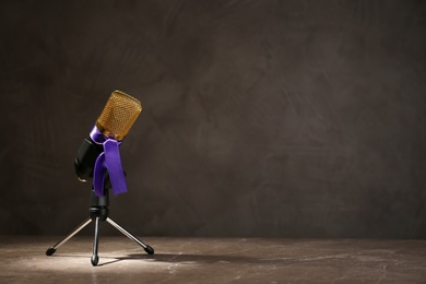 Photo of Microphone with purple awareness ribbon on wooden table against dark background, space for text
