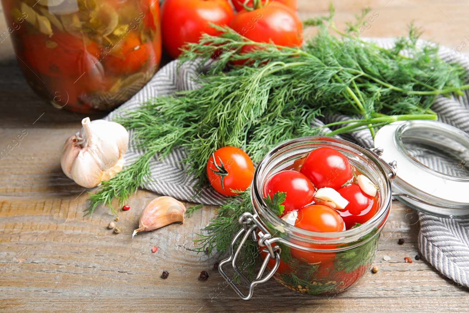 Photo of Pickled tomatoes in glass jars and products on wooden table