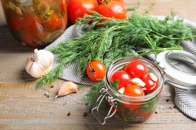 Photo of Pickled tomatoes in glass jars and products on wooden table