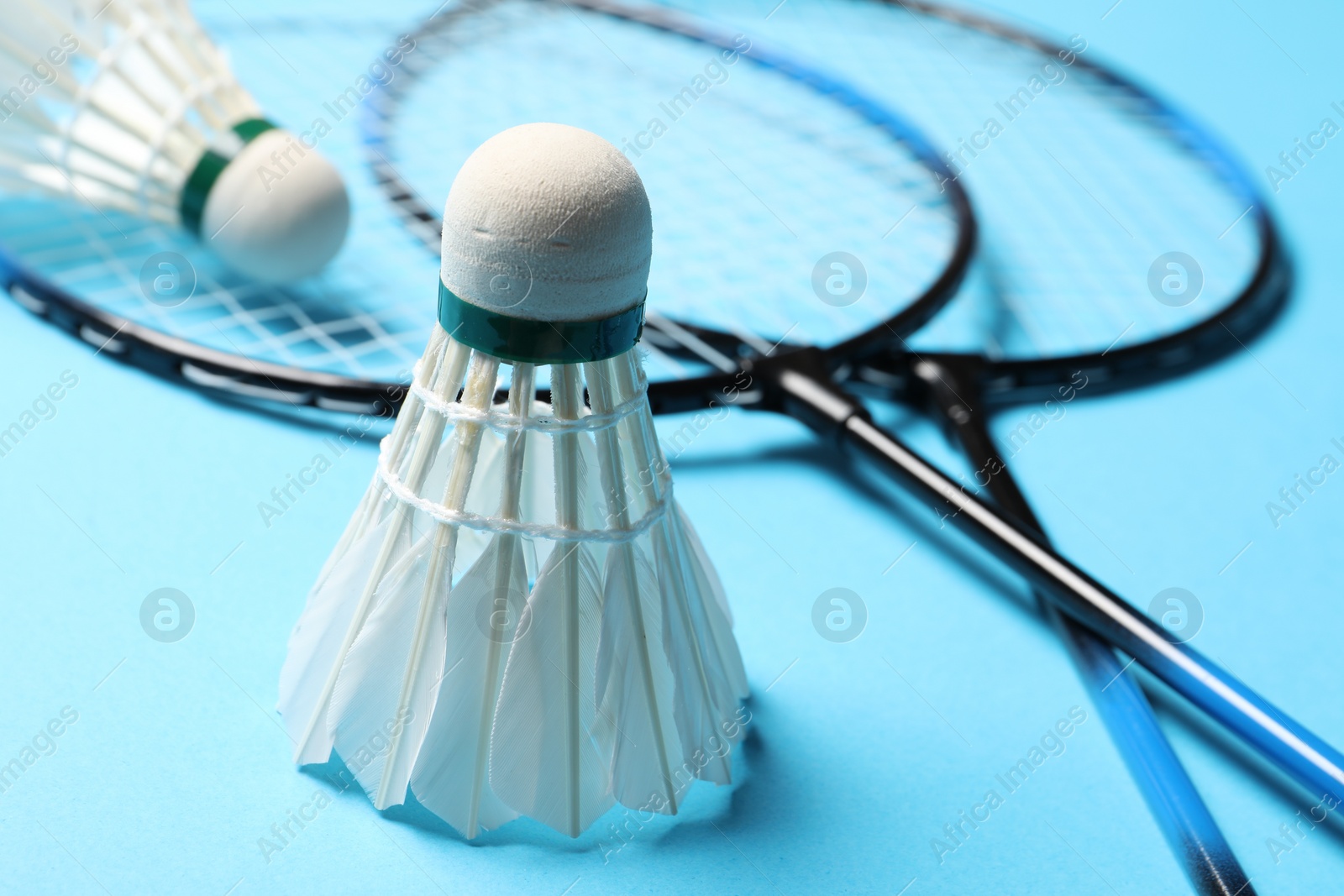 Photo of Feather badminton shuttlecocks and rackets on light blue background, closeup