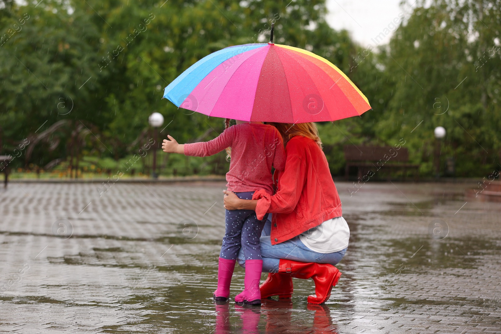 Photo of Mother and daughter with bright umbrella under rain outdoors