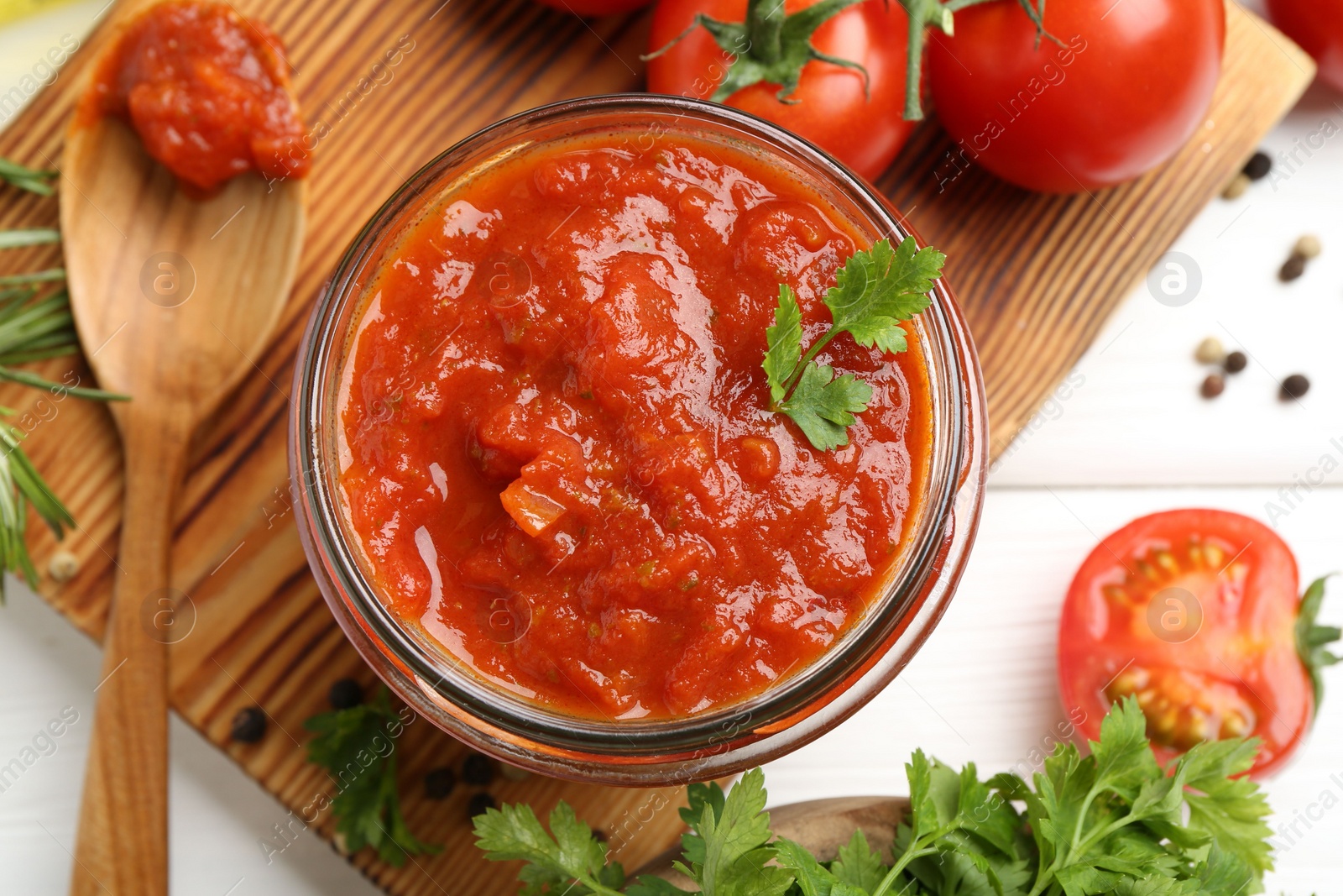 Photo of Homemade tomato sauce in jar, spoon and fresh ingredients on white wooden table, flat lay