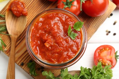 Photo of Homemade tomato sauce in jar, spoon and fresh ingredients on white wooden table, flat lay