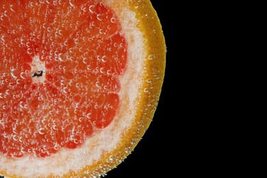 Slice of grapefruit in sparkling water on black background, closeup. Citrus soda