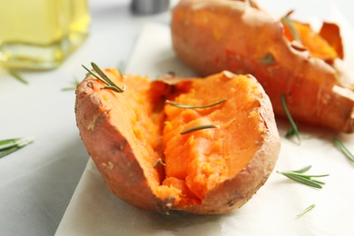 Photo of Delicious baked sweet potatoes with rosemary on parchment, closeup