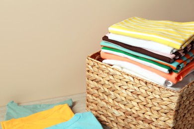 Photo of Wicker laundry basket with clean clothes on floor near beige wall, closeup