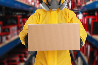 Image of Man wearing chemical protective suit with cardboard box in store, closeup. Wholesale market