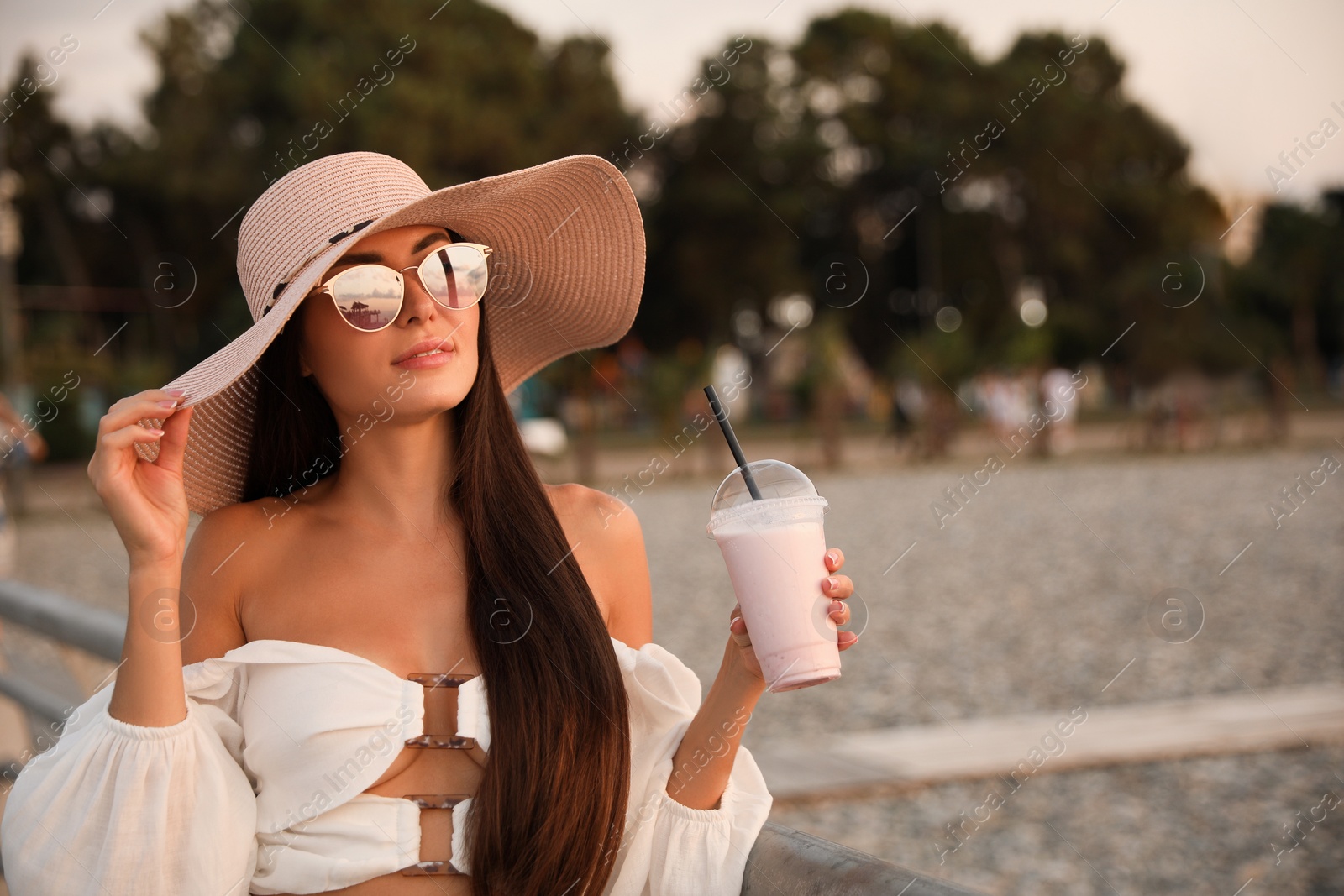 Photo of Beautiful young woman with tasty milk shake outdoors, space for text