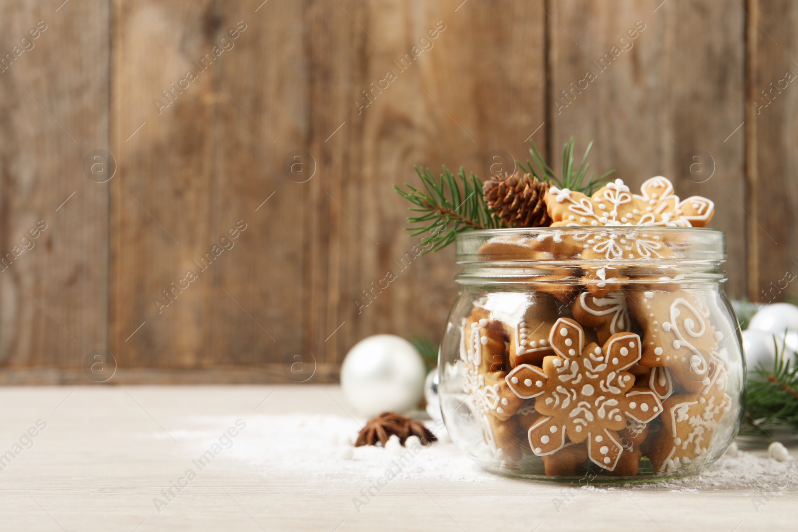 Photo of Tasty Christmas cookies in glass jar and festive decor on beige wooden table. Space for text