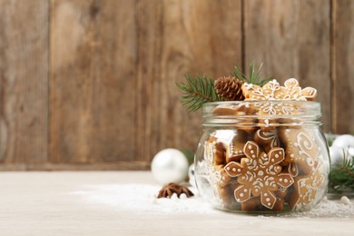 Tasty Christmas cookies in glass jar and festive decor on beige wooden table. Space for text