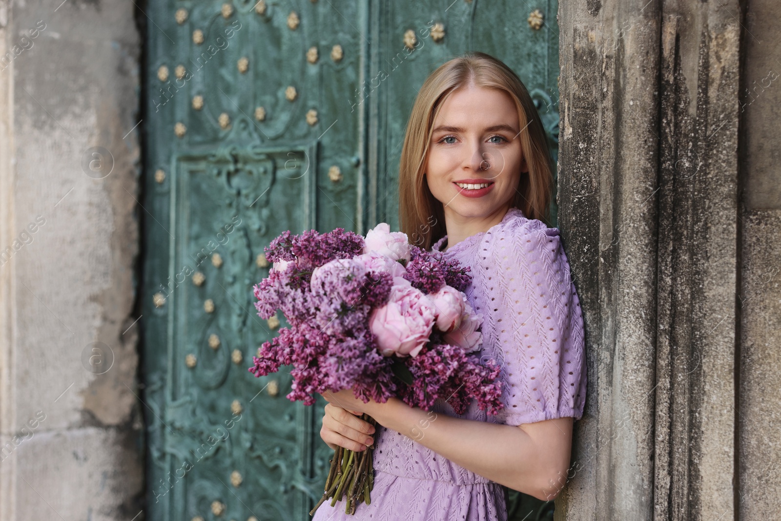 Photo of Beautiful woman with bouquet of spring flowers near building outdoors