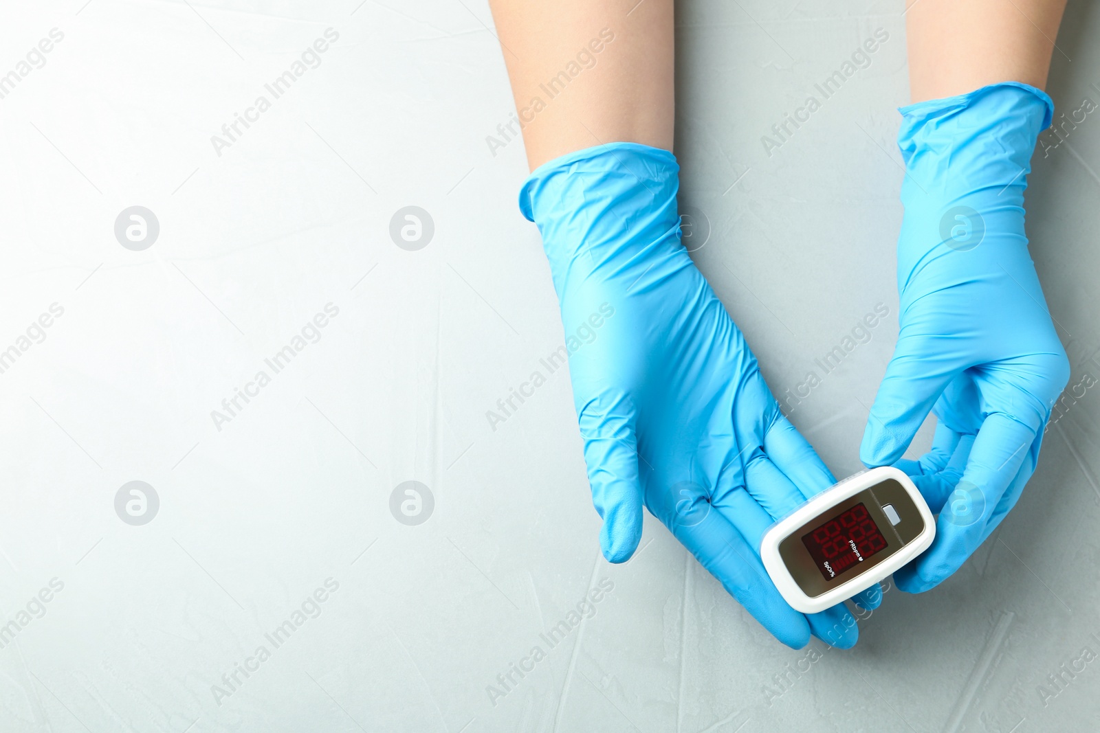 Photo of Doctor in latex gloves holding fingertip pulse oximeter on light grey stone background, top view. Space for text