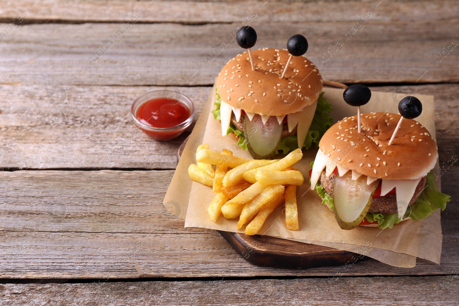 Photo of Cute monster burgers served with french fries and ketchup on wooden table, space for text. Halloween party food