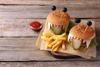 Photo of Cute monster burgers served with french fries and ketchup on wooden table, space for text. Halloween party food