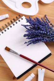 Photo of Bouquet of beautiful preserved lavender flowers, notebook, palette, brush and paints on wooden table, flat lay