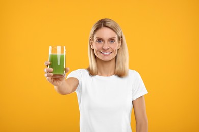 Photo of Happy woman with glass of fresh celery juice on orange background