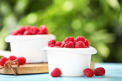 Photo of Bowls with delicious ripe raspberries on wooden table against blurred background, space for text