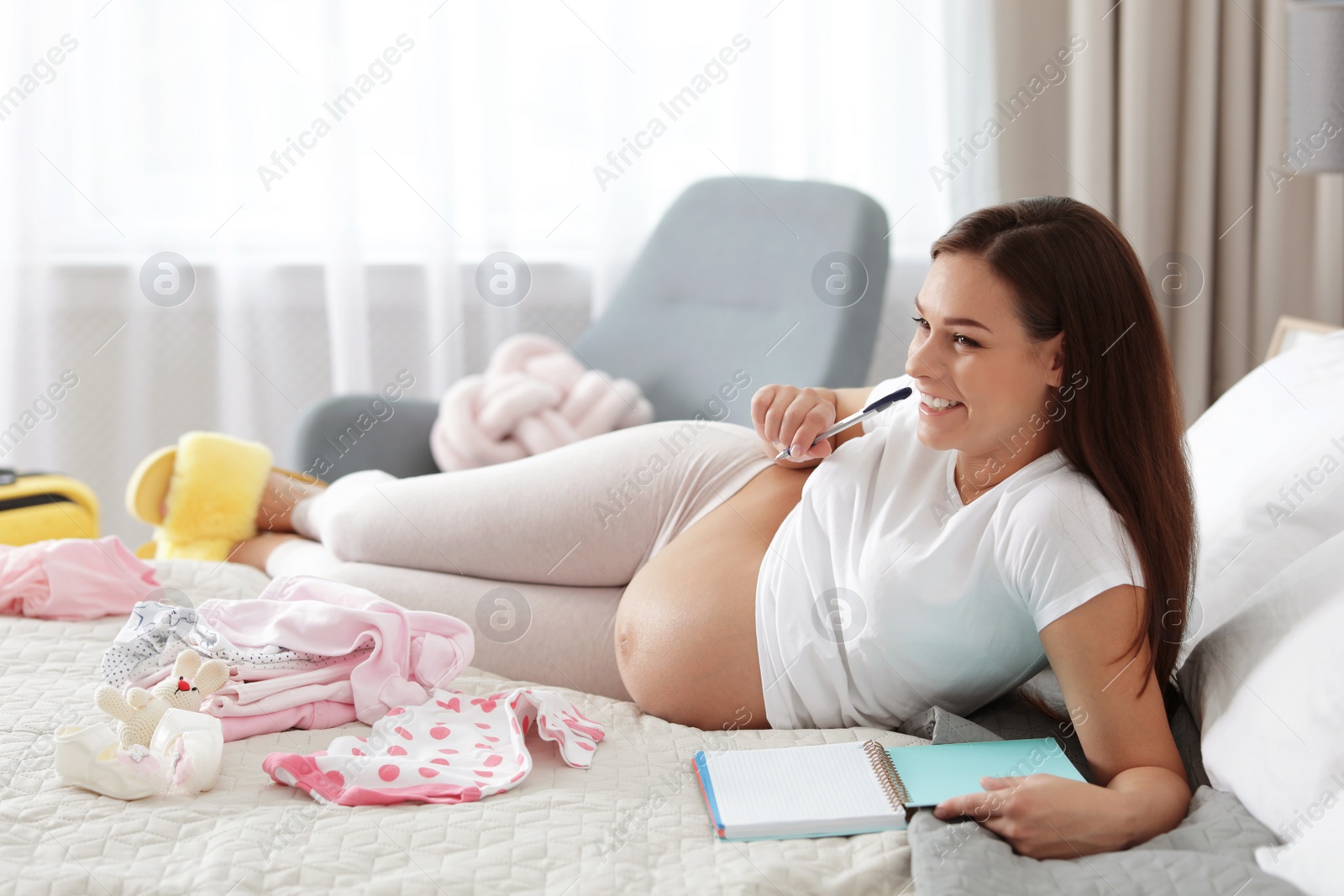 Photo of Pregnant woman writing packing list for maternity hospital on bed at home