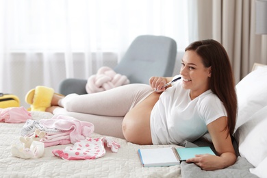 Photo of Pregnant woman writing packing list for maternity hospital on bed at home