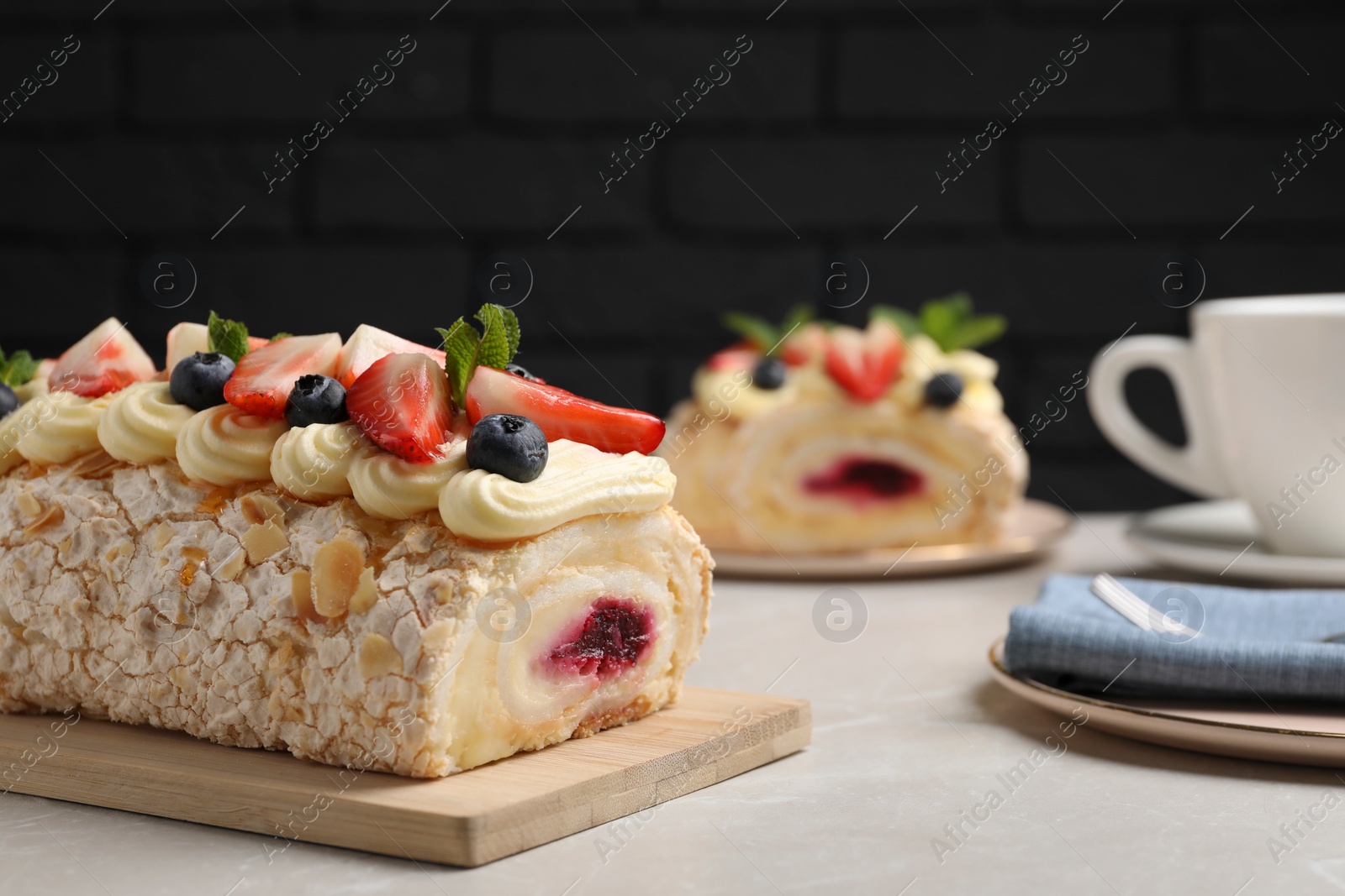 Photo of Tasty meringue roll with jam, cream, strawberry, blueberry and mint on light grey marble table. Space for text