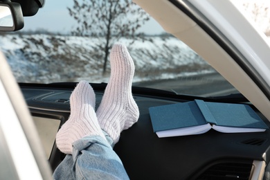 Photo of Young woman in warm socks holding her legs on car dashboard. Cozy atmosphere